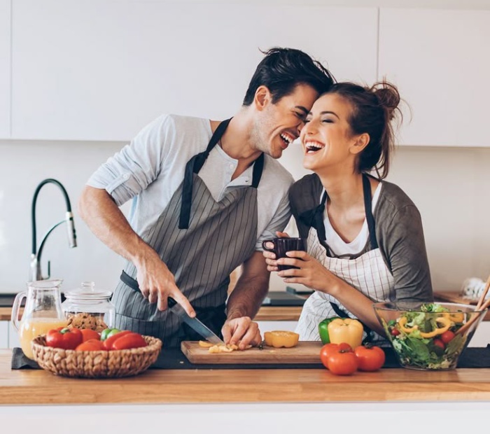 Couple cooking together in the kitchen, laughing and enjoying a romantic moment at home.