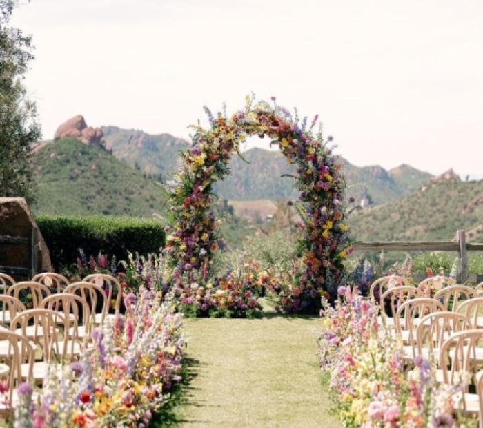 Garden wedding theme with a colorful floral arch, outdoor ceremony seating, blooming flowers along the aisle, and scenic mountain views.