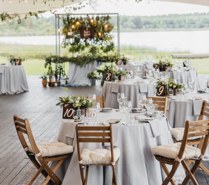Minimalist wedding theme with simple round tables, neutral linens, wooden chairs, greenery accents, and a clean elegant outdoor reception setup.