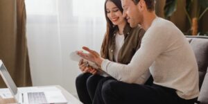 Newlywed couple sitting together at home reviewing financial documents and a laptop, smiling while planning their budget and future finances together.
