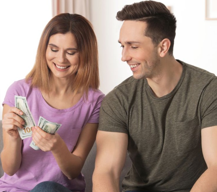 Couple sitting together at home counting cash and smiling, representing early investing and smart financial planning for the future.