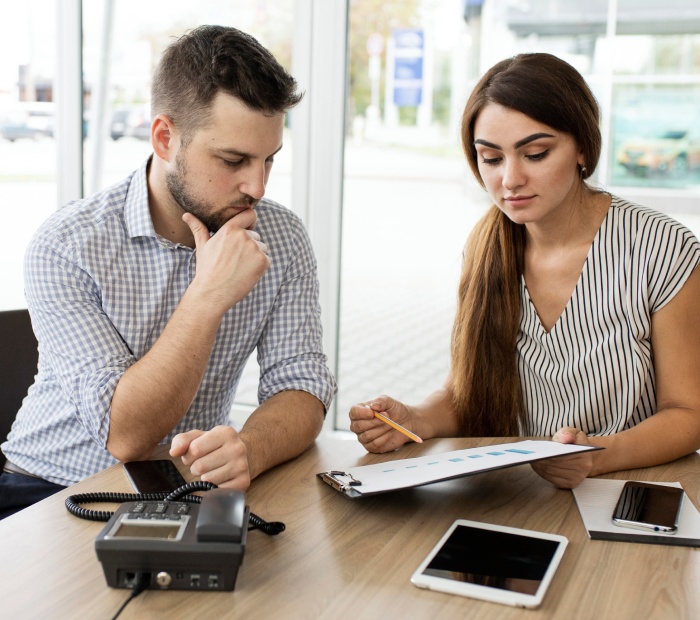 Couple sitting at a table discussing finances, reviewing a document with charts and notes, symbolizing open communication and financial planning together.