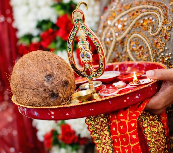 Traditional Bengali Bhaat ceremony ritual with a red puja thali holding a coconut, diya, kumkum, and rice, symbolizing blessings and prosperity before the wedding.
