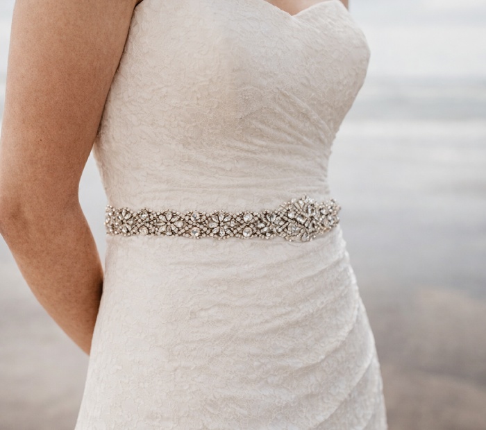 Close-up of a bride wearing an ivory lace wedding dress with a sparkling beaded belt at the waist.