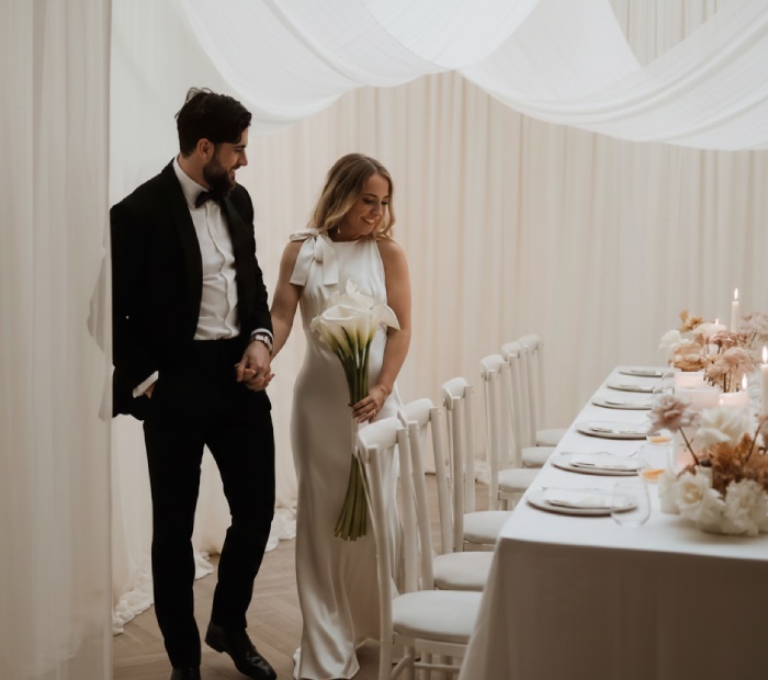 A bride and groom walk through a white draped venue.