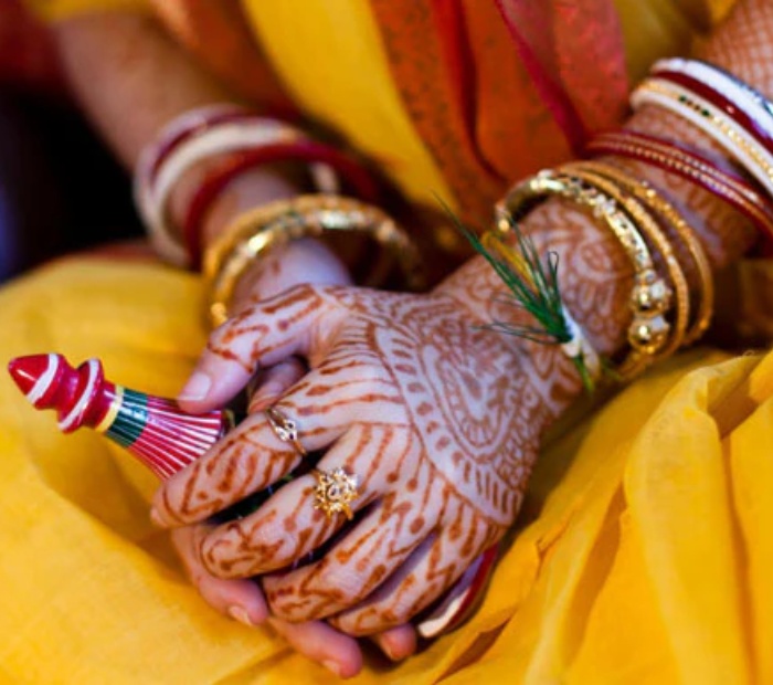 Close-up of bride’s hands wearing traditional Shankha Pola bangles with mehndi during a Bengali wedding ritual.