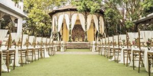 Wedding Venue Checklist: Questions, Costs & Capacity An outdoor wedding venue with a decorated wooden gazebo as a central altar, flanked by rows of gold Tiffany chairs on a green lawn.