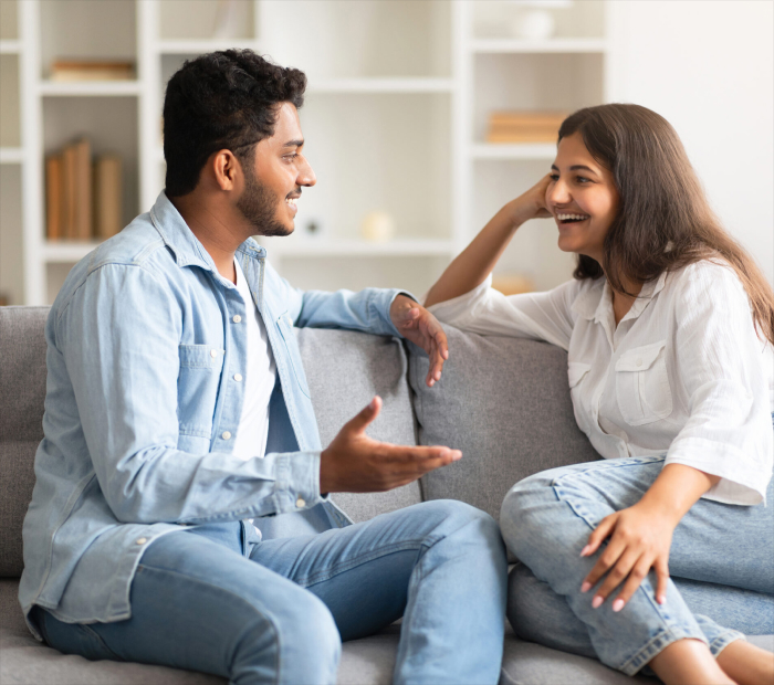 A couple sitting on a sofa smiling and talking openly, showing healthy communication and relationship understanding at home.