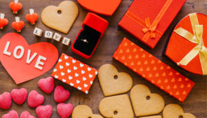50 Unique Valentine's Day Gifts for Your Special Someone An overhead shot of a wooden surface covered in Valentine's Day items, including heart-shaped cookies and candies, red gift boxes, a ring in a velvet box, and a paper heart with the word "LOVE."