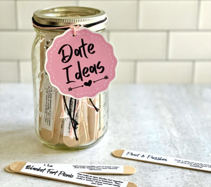 DIY Valentine’s gift jar labeled “Date Ideas” filled with popsicle sticks suggesting romantic activities, placed on a countertop.