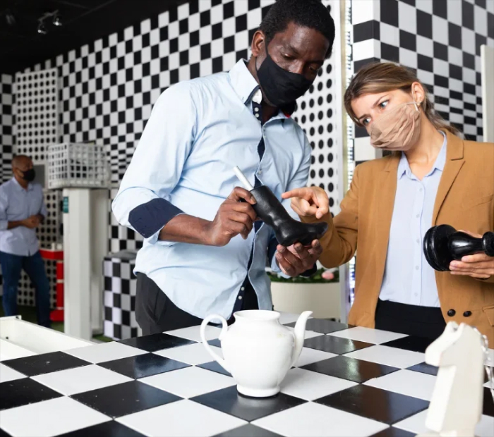 “Couple wearing masks examining chess pieces in an interactive exhibit.”