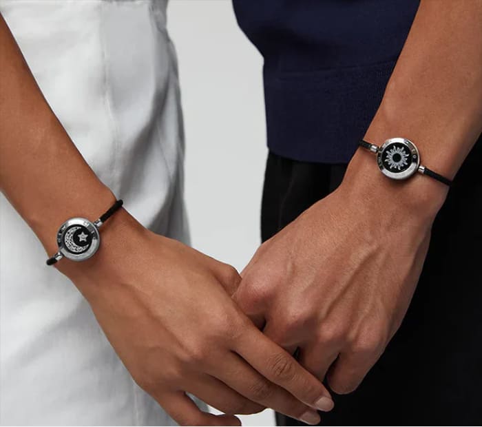 “Couple holding hands while wearing matching black couple bracelets.”