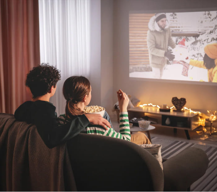 “Couple cuddling on a sofa while watching a movie at home with popcorn.”
