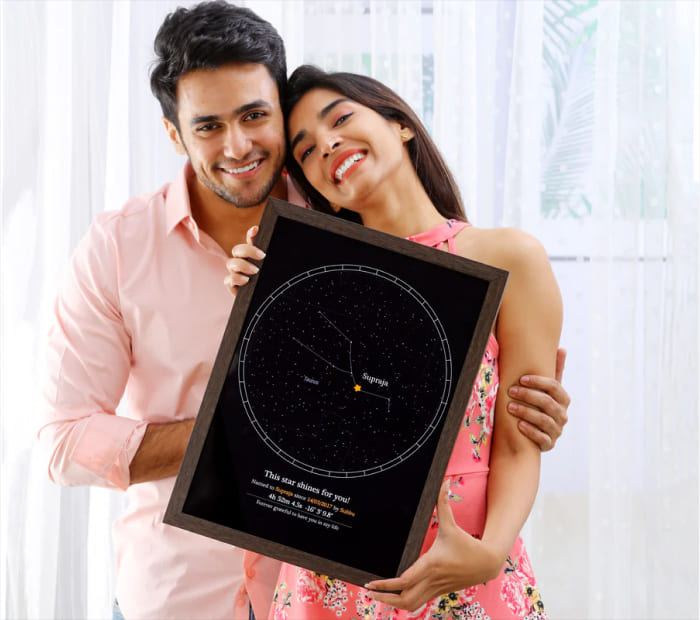 Smiling couple holding a framed personalized star map print with a night sky design, shown as a romantic Valentine’s Day gift.
