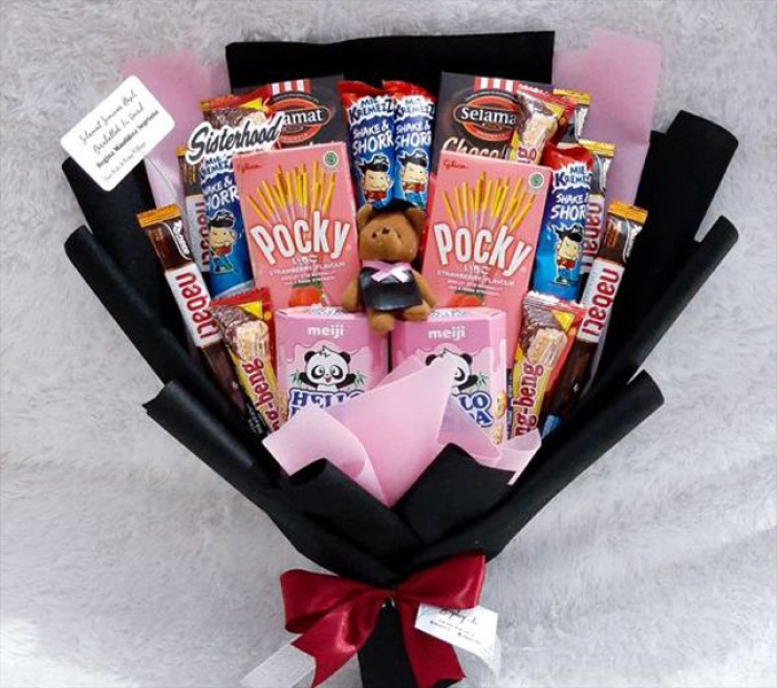 Valentine’s snack bouquet wrapped in black and pink paper, filled with chocolates, biscuits, and a small teddy bear, tied with a red ribbon.