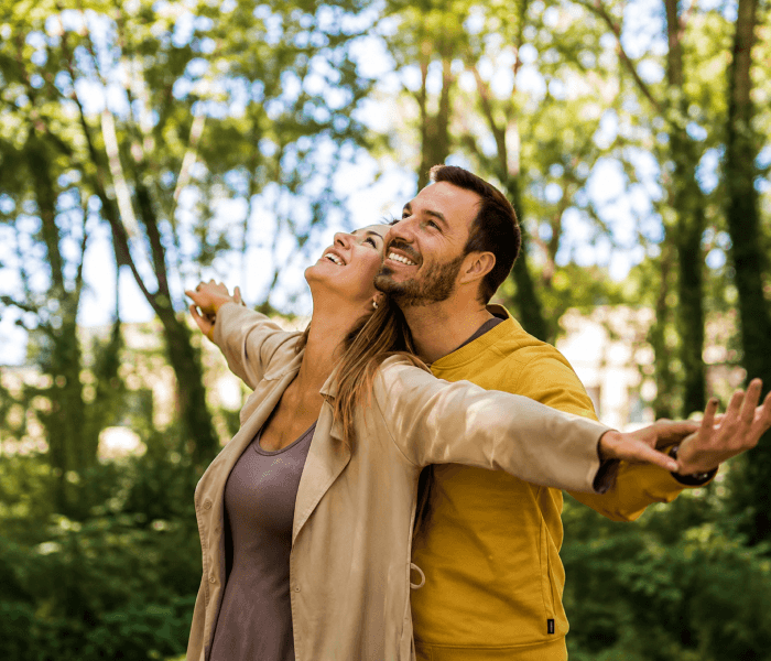 Being Yourself Feels Easy with Them - Happy Wedding App Couple embracing outdoors with arms outstretched in a sunny forest.