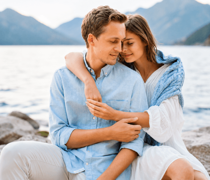 You Future Goals are Same - Happy Wedding App Couple sitting by a lake with mountains in the background; the woman hugs the man from behind, both looking serene.