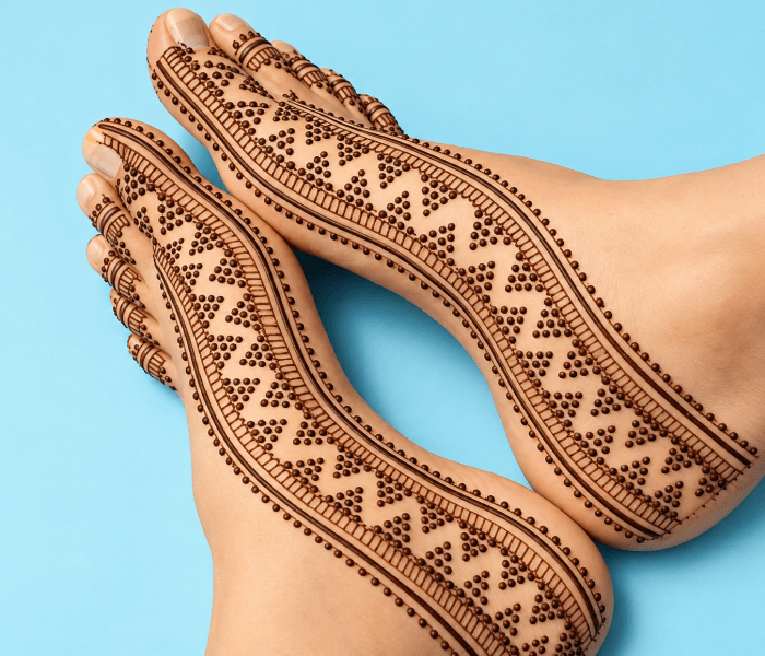 Dotted border - Happy Wedding App Feet adorned with intricate henna patterns on a blue background, showcasing mehndi designs along the arches and toes.