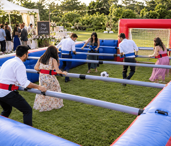 Musical Chairs for Adults - Happy Wedding App Adults playing human foosball inside an inflatable court on a grassy lawn.