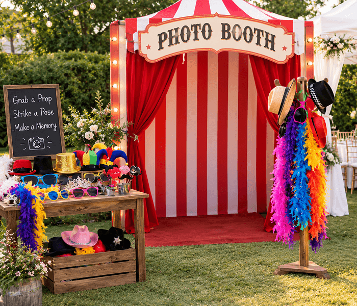 Photo Booth with Carnival Props - Happy Wedding App A red-and-white striped photo booth setup with colorful props, hats, and feather boas.