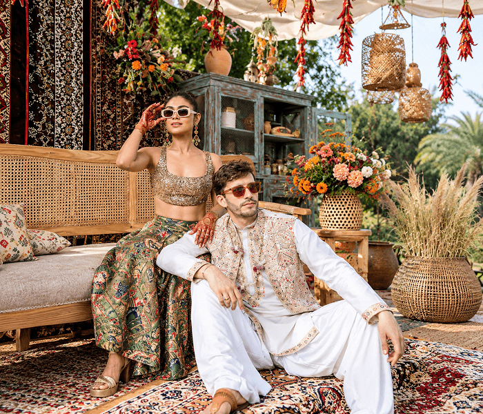 Regional Cultural Fusion Carnival - Happy Wedding App A couple in traditional Indian attire sitting on printed rugs near woven furniture, surrounded by festive decor.
